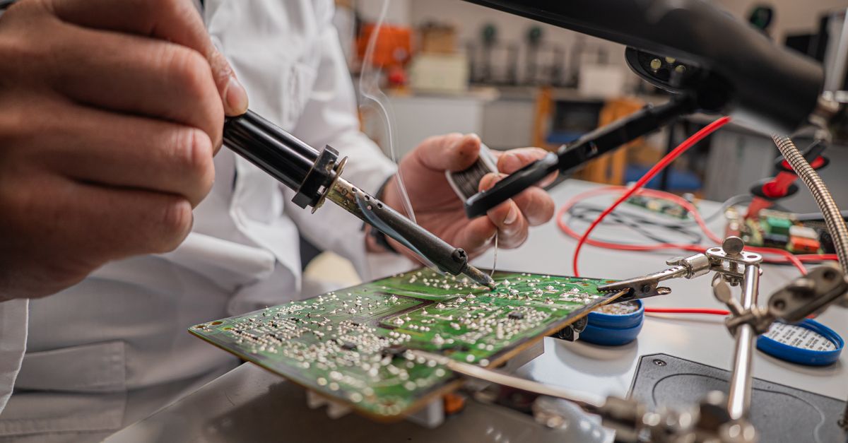 Technician's hands soldering a circuit board at a repair bench